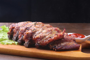 grilled barbecued ribs with lettuce leaves, hot chili pepper and sauce on wooden cutting board.