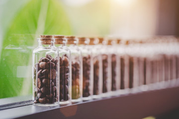 Coffee beans in glass bottles lined up in rows with leaves are the background, Warm light.