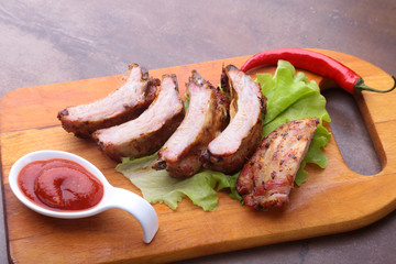 grilled barbecued ribs with lettuce leaves, hot chili pepper and sauce on wooden cutting board.