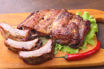 grilled barbecued ribs with lettuce leaves, hot chili pepper and sauce on wooden cutting board.