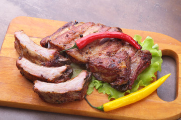 grilled barbecued ribs with lettuce leaves, hot chili pepper and sauce on wooden cutting board.