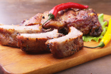 grilled barbecued ribs with lettuce leaves, hot chili pepper and sauce on wooden cutting board.