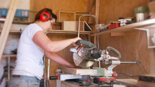 Woman sawing a wood board with a circular saw.