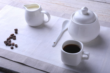 Cup of hot coffee espresso, coffee beans, jug of milk, and bowl with sugar on white background for copy space. Coffee concept.