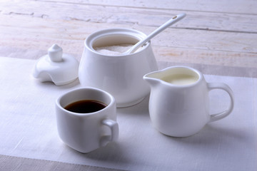 Cup of hot coffee espresso, coffee beans, jug of milk, and bowl with sugar on white background for copy space. Coffee concept.