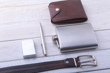 Gadgets and accessories for men on light wooden background. Fashionable men s belt, wallet, lighter, Stainless hip flask and pen.