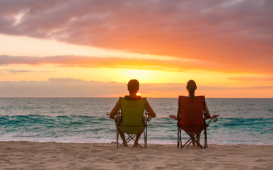 Fototapeta na wymiar Young couple sitting on the beach relaxing watching the colorful sunset. 