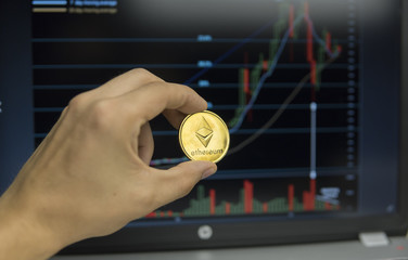 Male businessman hand holding Ethereum coin on a background of growth graph on a screen of laptop. Virtual money and Financial growth concept on chart background. Trading Mining of Ethereums.