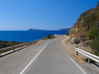 Empty asphalt road winds along coastline of breathtaking Sardinia on sunny day.