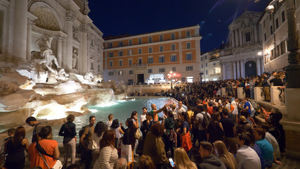 Masses of people taking photos of the beautiful Fontana di Trevi at night.