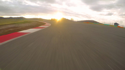 POV: Driving a fast car along the scenic asphalt racetrack on a cloudy evening.