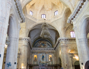 Fototapeta premium Interior of Old Havana Catholic Cathedral. The hall has stone pillars, high roof, and rows of benches going til the far end.