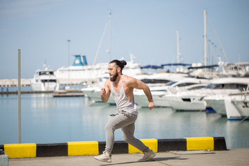 Caucasian sportsman jogging on ocean pier or waterfront with anchored yachts, working out in summer morning.