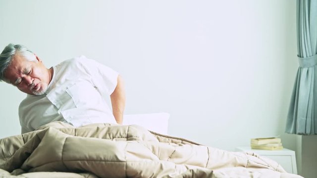 Senior man in bed trying to get up and nurse helping him. Old asian man and beautiful asian nurse woman in bedroom and open curtain. Senior home service concept. Front shot.