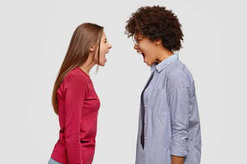 Interracial rival concept. Furious angry two desperate women scream loudly at each other, have...