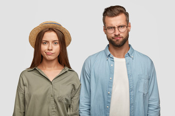 Indoor shot of sullen displeased family couple purse lips with unpleasant look, have to pay much money during vacation, express negative emotions, isolated over white background. Relationships concept