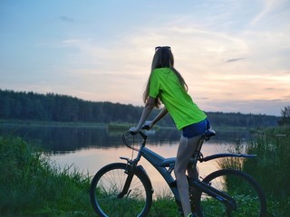 Polonne / Ukraine - 14 September 2018: The girl on a bike looks at the sunset on the lake