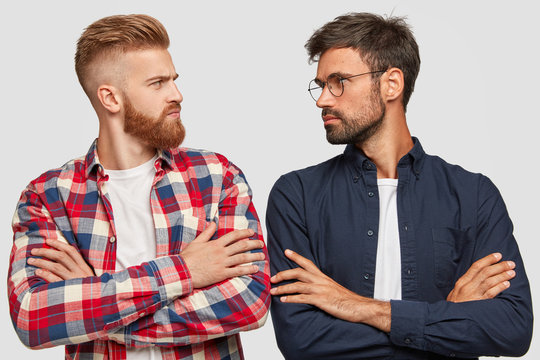 Photo of serious male opponents stand crossed hands, look at each other, have competiton, stand shoulder to shoulder against white background, ready to rival. People and relationships concept
