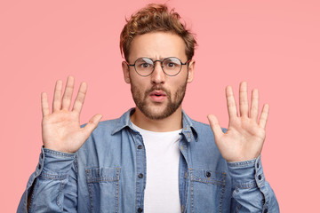 Calm down, please! Handsome unshaven Caucasian man keeps palms in front, asks to leave him in peace...