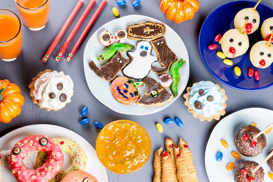 Halloween sweet treats, party food concept. Scary cookies, monster biscuits and fruits on grey background.