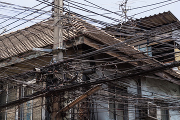 Messy electrical cables unsafe near old house.
