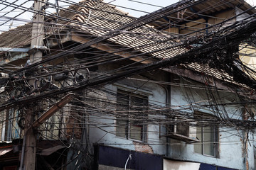 Messy electrical cables unsafe near old house.