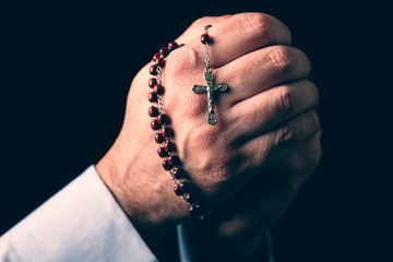 Male hands praying holding a rosary with Jesus Christ in the cross or Crucifix on black background. Mature man with Christian Catholic religious faith - obrazy, fototapety, plakaty