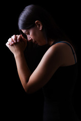 Faithful woman praying, hands folded in worship to god with head down and eyes closed in religious fervor, on a black background. Concept for religion, faith, prayer and spirituality.