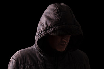 Scary and creepy caucasian or white man hiding in the shadows, with the face and identity hidden with the hood, and standing in the darkness. Low key, black background. Concept for fear, danger,