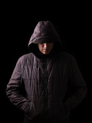 Naklejka na ściany i meble Scary and creepy caucasian or white man hiding in the shadows, with the face and identity hidden with the hood, and standing in the darkness. Low key, black background. Concept for fear, danger,