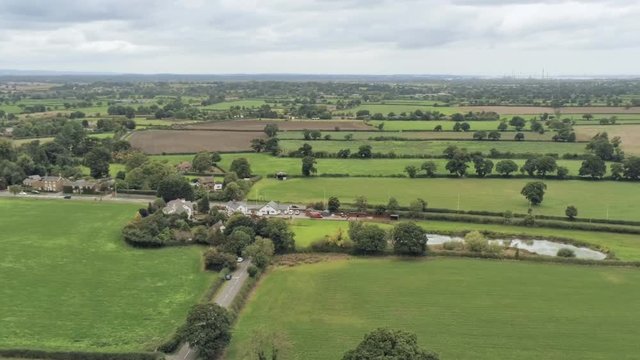 Aerial view, slow panning move. Plains, houses, pond in Cheshire. Cars on road in background