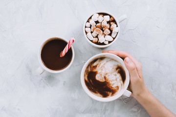 Three cups of vegan hot chocolate or cocoa with different toppings on grey