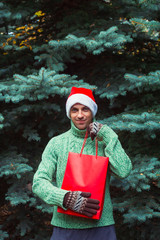 Obraz premium man in a green sweater and Santa Claus red hat with red gift package