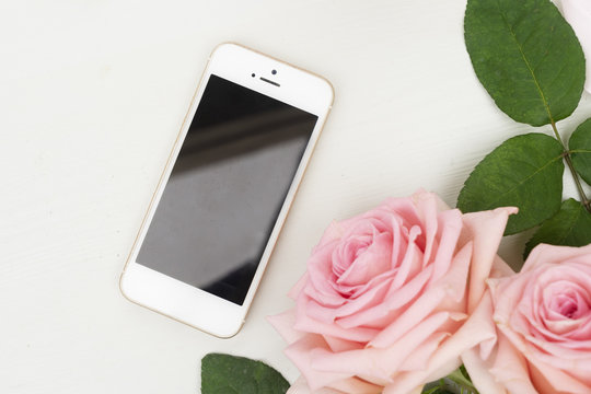 Two Rose Fresh Flowers On Table With White Phone From Above With Copy Space, Flat Lay Scene