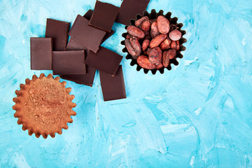 Cocoa beans background on blue table. Dark chocolate pieces