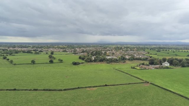 Aerial view, slow zoom in move. Tarvin small town among plains in Cheshire. Rain over hills in background