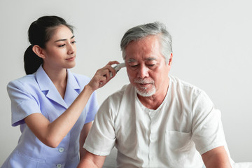 Beautiful nurse using high tech Temperature measurement tool on old man.