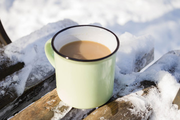 green cup of coffee on wooden rustic bench in the winter forest.