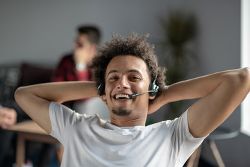 Satisfied relaxed african-american freelancer feeling happy at work sitting at office desk with headset.