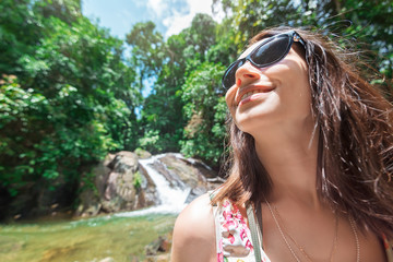 girl on waterfall in sunny day/ Happy joyful girl tourist in sunglasses on vacation against the background of a small waterfall in sunny day