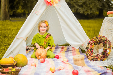 Little girl lying and playing in a tent, children's house wigwam in park Autumn portrait of cute curly girl. Harvest or Thanksgiving. autumn decor, party, picnic. Child in halloween costume. © MartaKlos