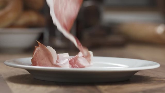 Slow motion prosciutto falling on white plate