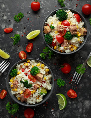Fresh Tuna rice salad with sweet corn, cherry tomatoes, broccoli, parsley and lime in black bowl