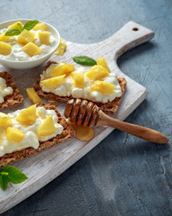 Homemade Crispbread toast with Cottage Cheese, Pineapple and honey on white wooden board.