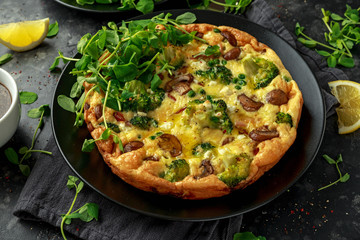 Homemade Frittata with mushrooms, broccoli, feta cheese, green peas and bacon on black plate