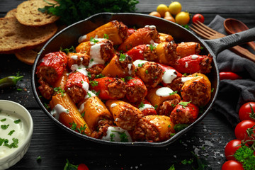 Sausage meat, mince and rice Stuffed sweet mini bell peppers baked in cast iron skillet, pan topped with yogurt and fresh parsley