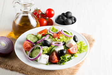 Fresh Greek salad made of cherry tomato, ruccola, arugula, feta, olives, cucumbers, onion and spices. Caesar salad in a white bowl on wooden background. Healthy organic diet food concept.