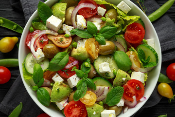 Healthy low calories salad with lettuce, heirloom tomatoes, avocado, feta cheese, red onion, cucumber, sweet peas, olives, thyme, mint and basil.