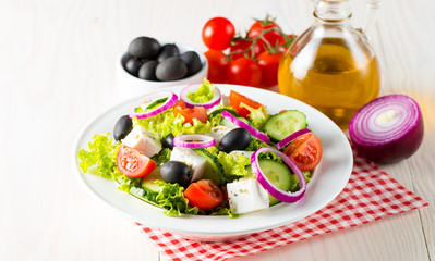 Fresh Greek salad made of cherry tomato, ruccola, arugula, feta, olives, cucumbers, onion and spices. Caesar salad in a white bowl on wooden background. Healthy organic diet food concept.