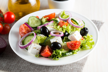 Fresh Greek salad made of cherry tomato, ruccola, arugula, feta, olives, cucumbers, onion and spices. Caesar salad in a white bowl on wooden background. Healthy organic diet food concept.